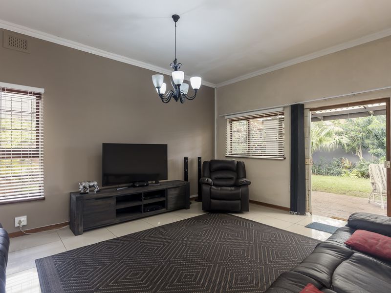 A comfortable living room featuring tiled floors, a central chandelier, and a sliding glass door providing direct access to the rear garden.