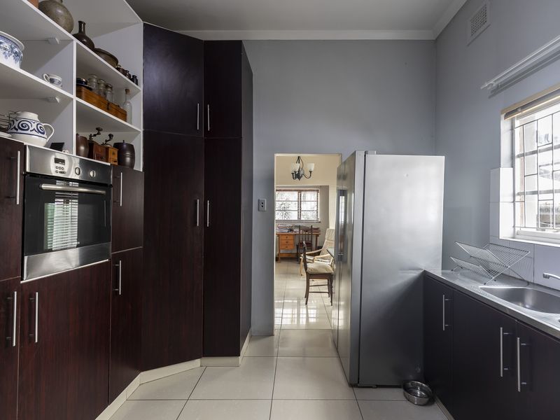 A functional kitchen featuring dark wood cabinetry, built-in oven, stainless steel sink, and tiled flooring, with a view through to the adjacent living area.