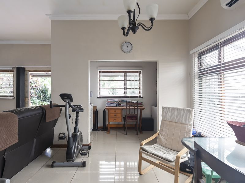 A bright living area featuring tiled flooring, large windows with venetian blinds, and an integrated air conditioning unit.