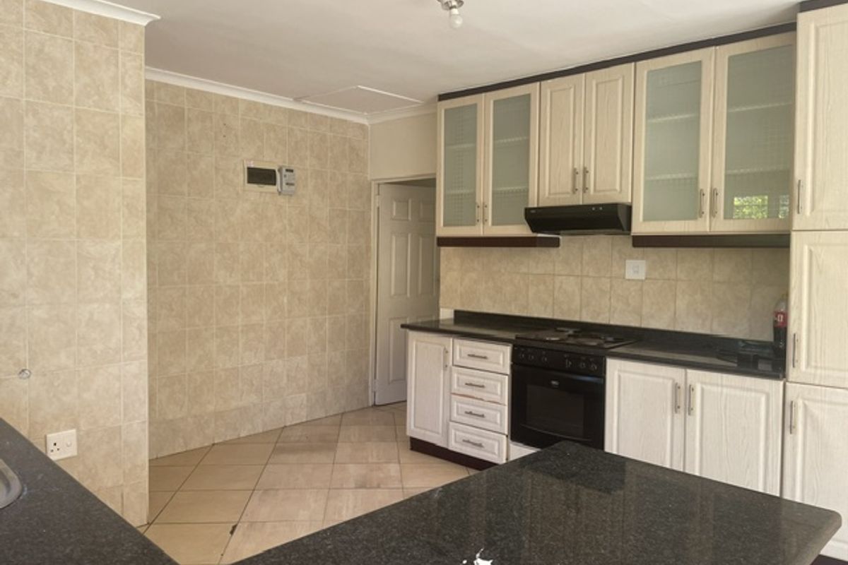 A functional kitchen featuring built-in cabinetry, granite countertops, an integrated oven and hob, and tiled splashbacks throughout.