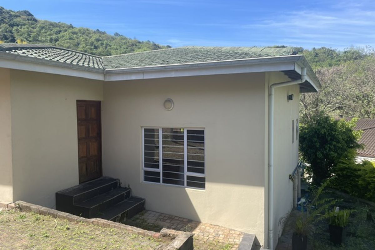 Rear exterior view of the cottage featuring a tiled roof, timber entrance door, aluminium windows with security bars, and paved access steps.