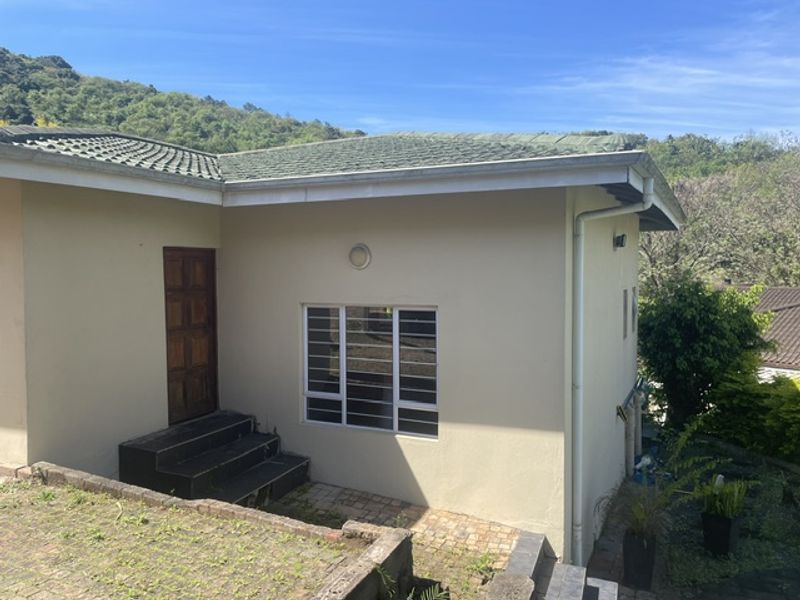 Rear exterior view of the cottage featuring a tiled roof, timber entrance door, aluminium windows with security bars, and paved access steps.