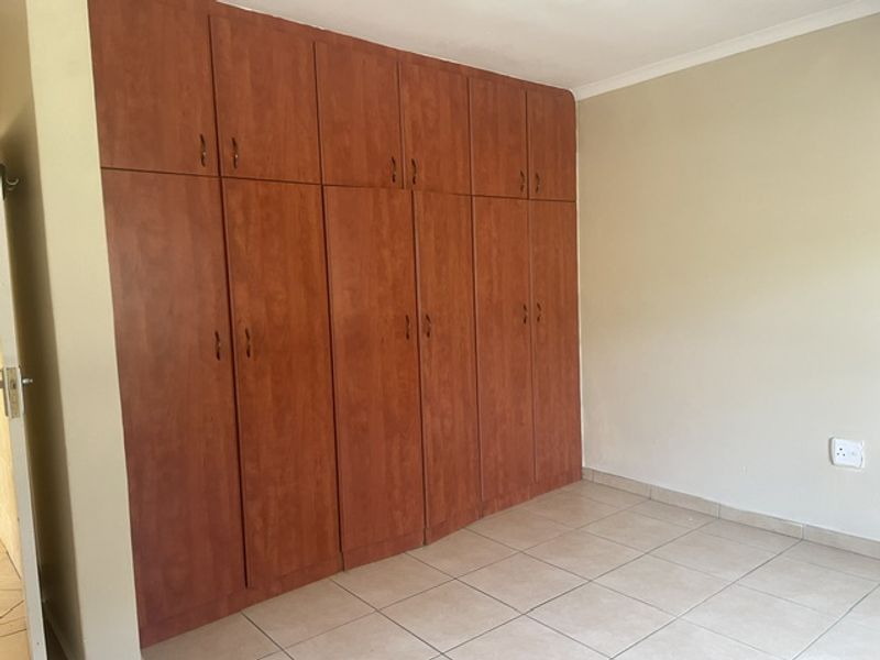 A clean, empty bedroom featuring extensive floor-to-ceiling built-in wooden cupboards and neutral tiled flooring.