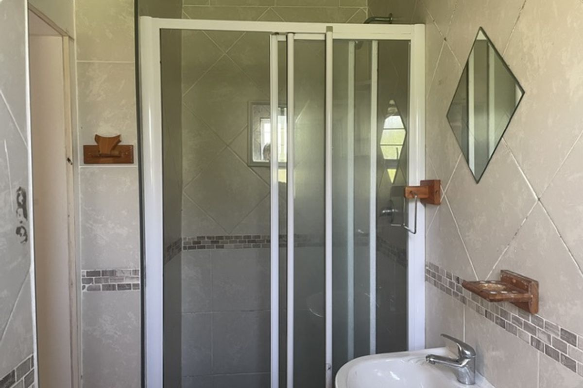 A compact bathroom featuring a shower enclosure, pedestal basin with chrome mixer, and neutral ceramic wall tiling with decorative mosaic accents.