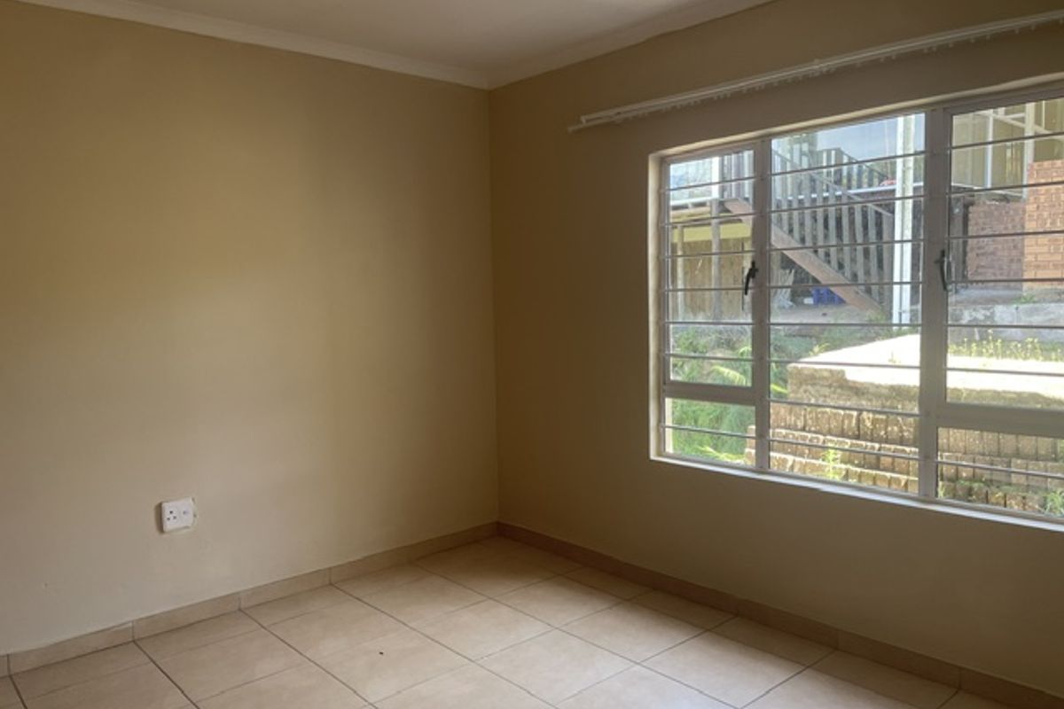 An empty bedroom featuring neutral wall paint, tiled flooring, and a large window fitted with security bars.