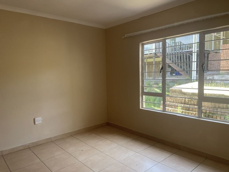 An empty bedroom featuring neutral wall paint, tiled flooring, and a large window fitted with security bars.