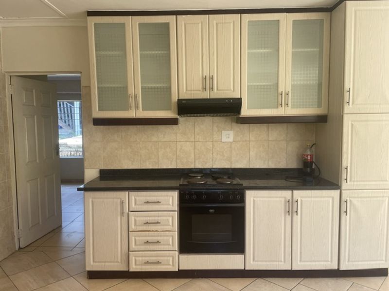 A functional kitchen featuring built-in cabinetry, a stone countertop, an electric hob, and an integrated oven with a tiled backsplash.