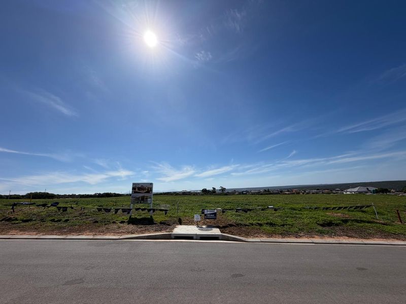 A vacant residential plot of land featuring a clear street frontage, concrete curb, and stormwater drainage infrastructure, ready for development.