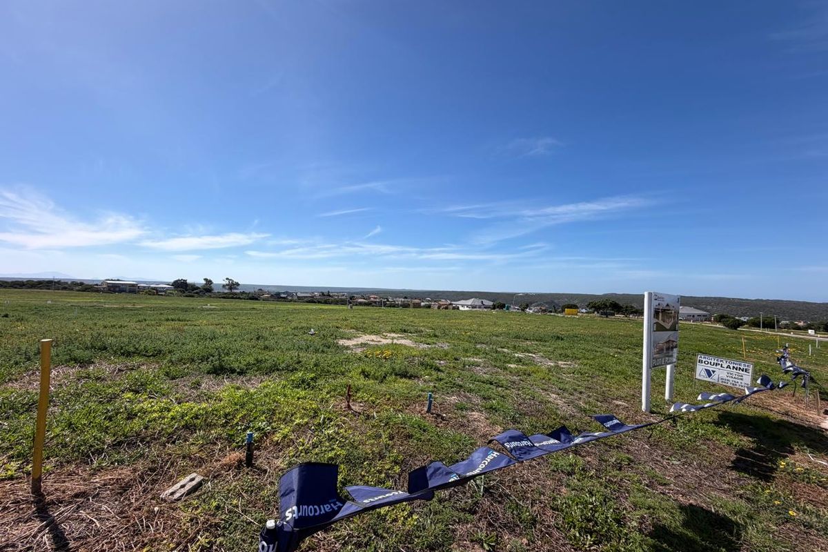 A wide-angle view of a vacant residential plot featuring natural vegetation and a real estate sign, ready for development.