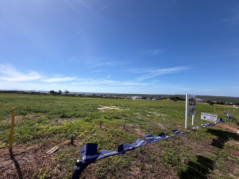 A wide-angle view of a vacant residential plot featuring natural vegetation and a real estate sign, ready for development.