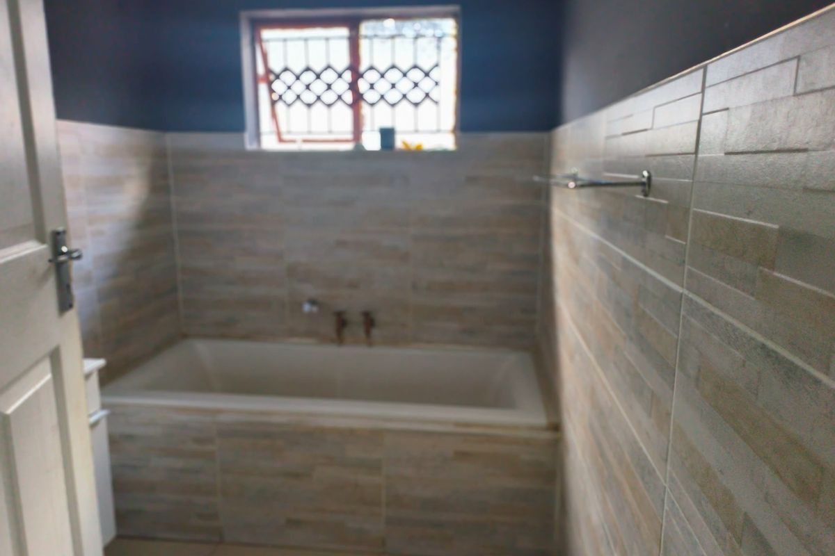 A functional bathroom featuring a built-in bathtub, tiled wall finishes, and a window with security bars.