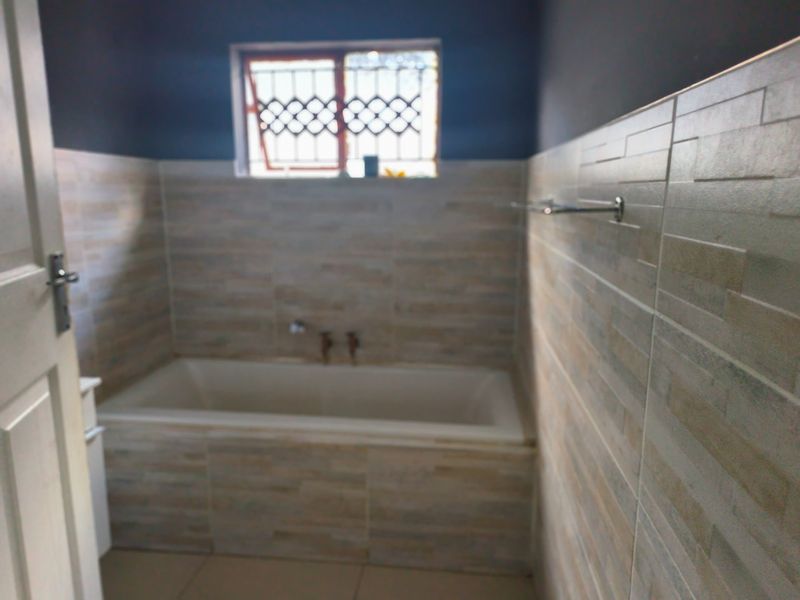 A functional bathroom featuring a built-in bathtub, tiled wall finishes, and a window with security bars.