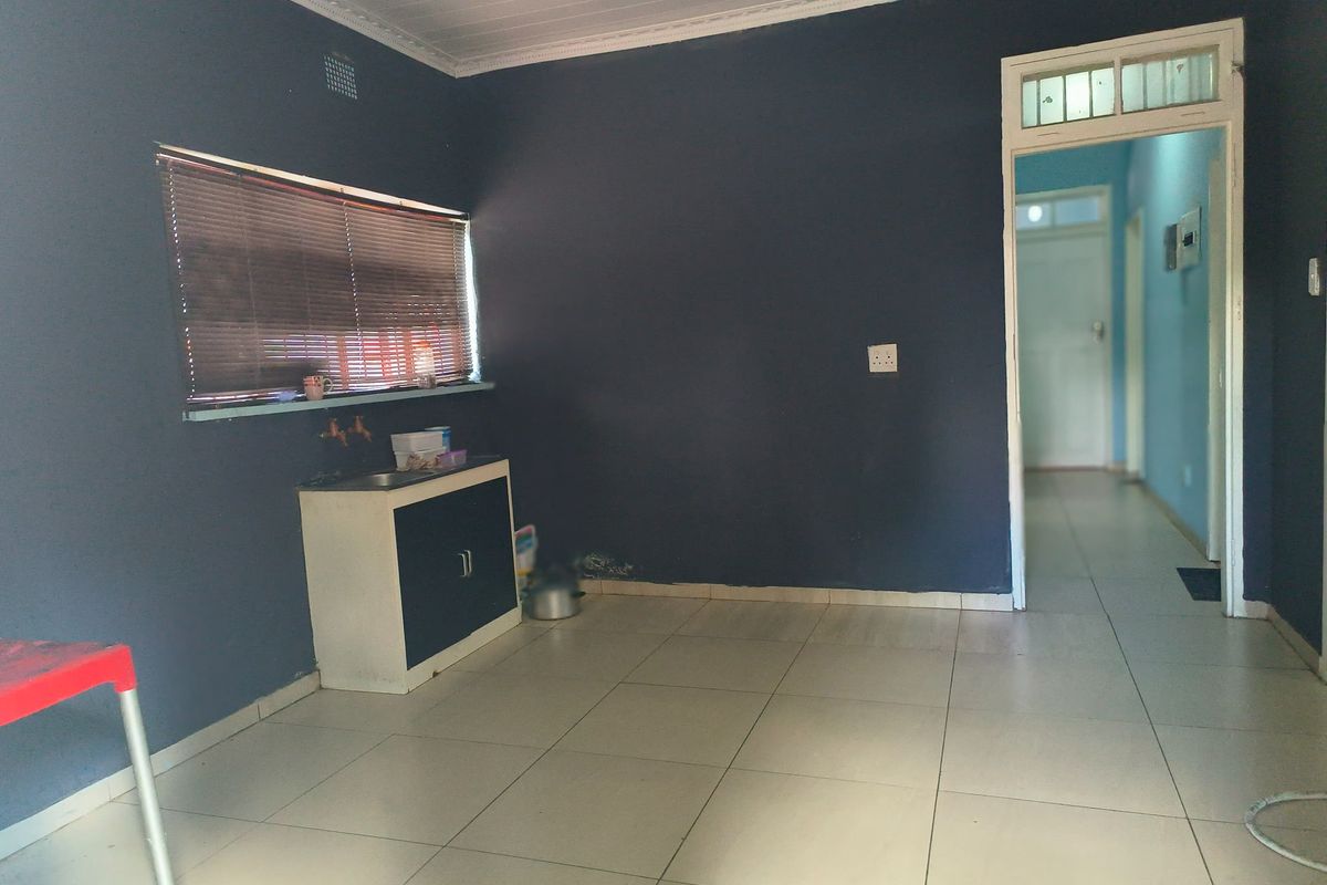 A basic kitchen area featuring tiled flooring, a small built-in sink cabinet, and dark painted walls, leading into a hallway.