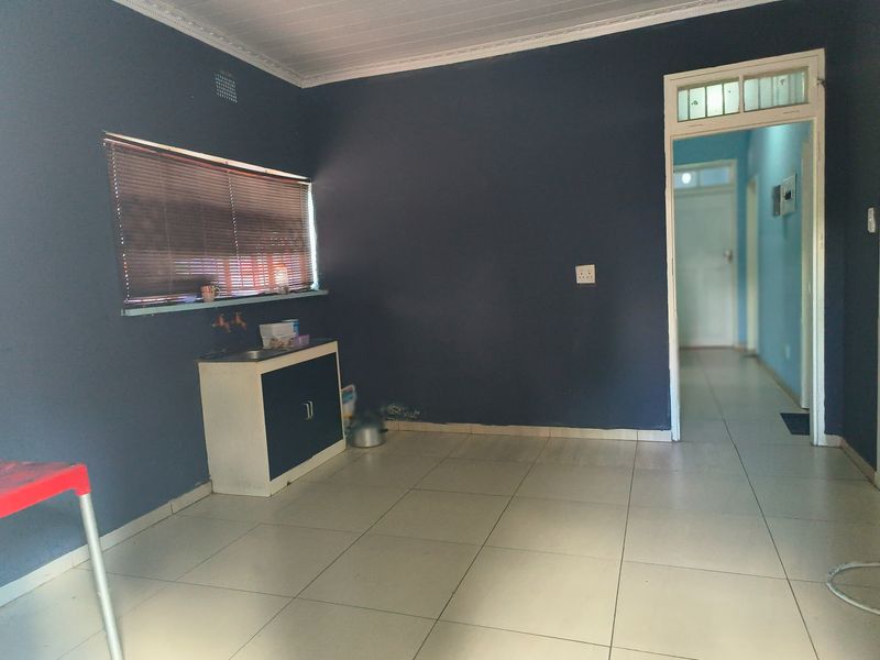 A basic kitchen area featuring tiled flooring, a small built-in sink cabinet, and dark painted walls, leading into a hallway.
