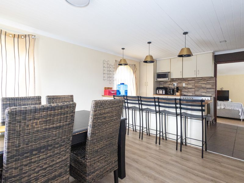Open plan kitchen and dining area featuring built-in cabinetry, a stone-look backsplash, and modern pendant lighting over the breakfast bar.