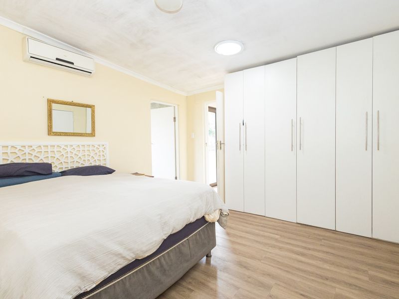 Spacious bedroom featuring extensive built-in white cabinetry, laminate flooring, and a wall-mounted split-system air conditioning unit.