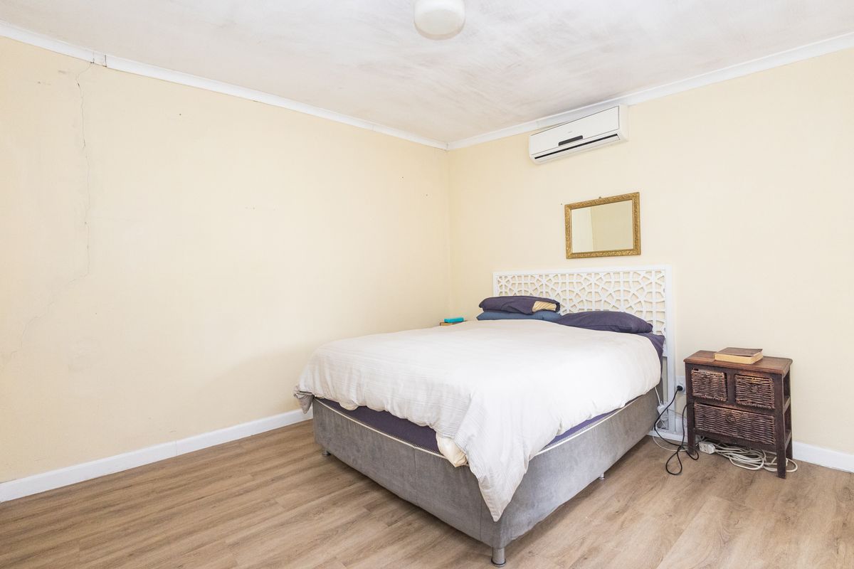 A bedroom featuring laminate flooring and a wall-mounted air conditioning unit, showing signs of wear including a visible crack on the wall.