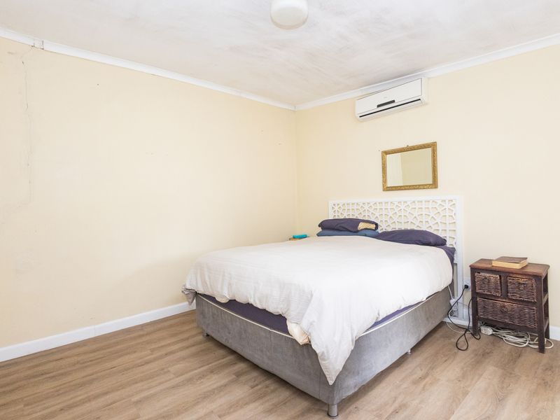 A bedroom featuring laminate flooring and a wall-mounted air conditioning unit, showing signs of wear including a visible crack on the wall.