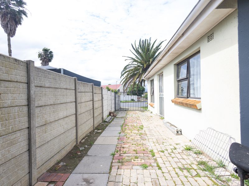 Side exterior walkway featuring paved path, precast concrete boundary wall, and secure metal gate access.