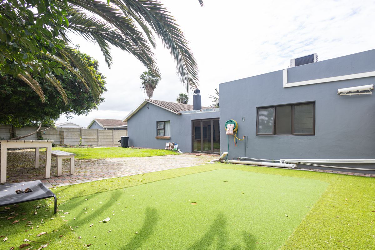 Rear exterior view featuring a paved patio area, artificial lawn, and direct access to the home via sliding glass doors.