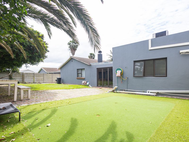 Rear exterior view featuring a paved patio area, artificial lawn, and direct access to the home via sliding glass doors.