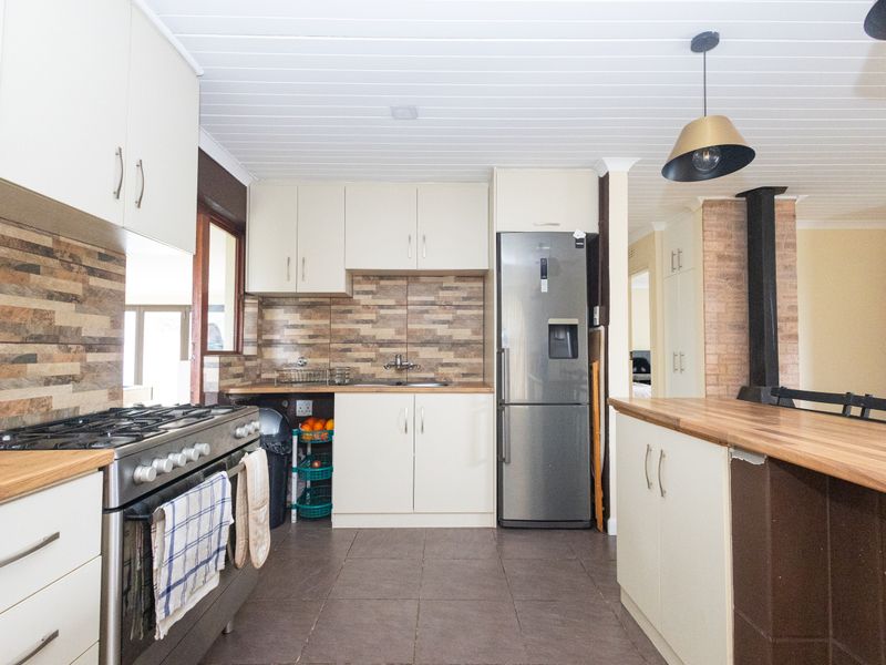 A well-maintained kitchen featuring cream cabinetry, stone tile backsplash, wood-look countertops, a gas stove, and an integrated wood-burning fireplace.