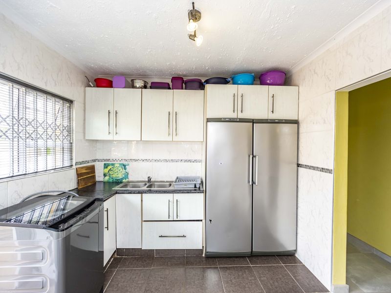 A functional scullery area featuring built-in cabinetry, double sink, tiled finishes, and a window with security bars.