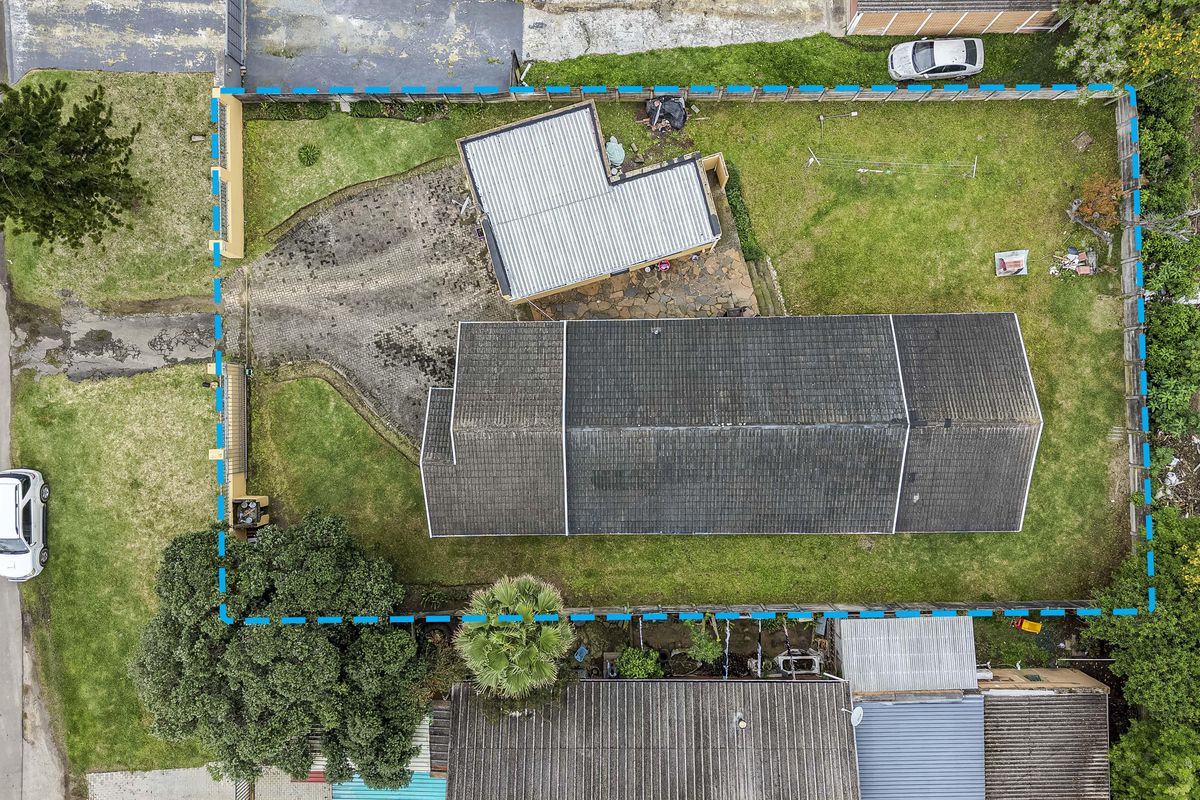 Aerial view of the property showing the main house, detached outbuilding, paved driveway, and surrounding garden area within the fenced boundary.