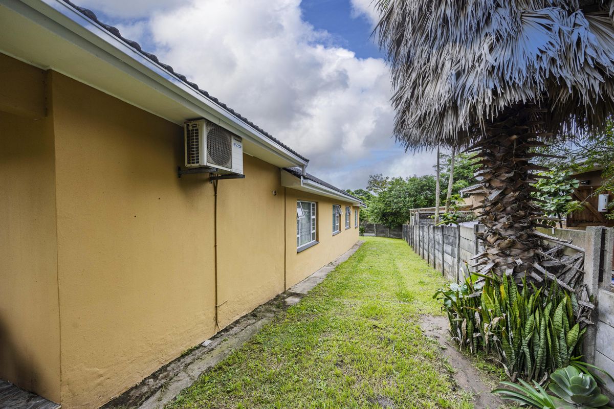A view of the rear exterior of the house featuring a lawn, boundary wall, and wall-mounted air conditioning unit.