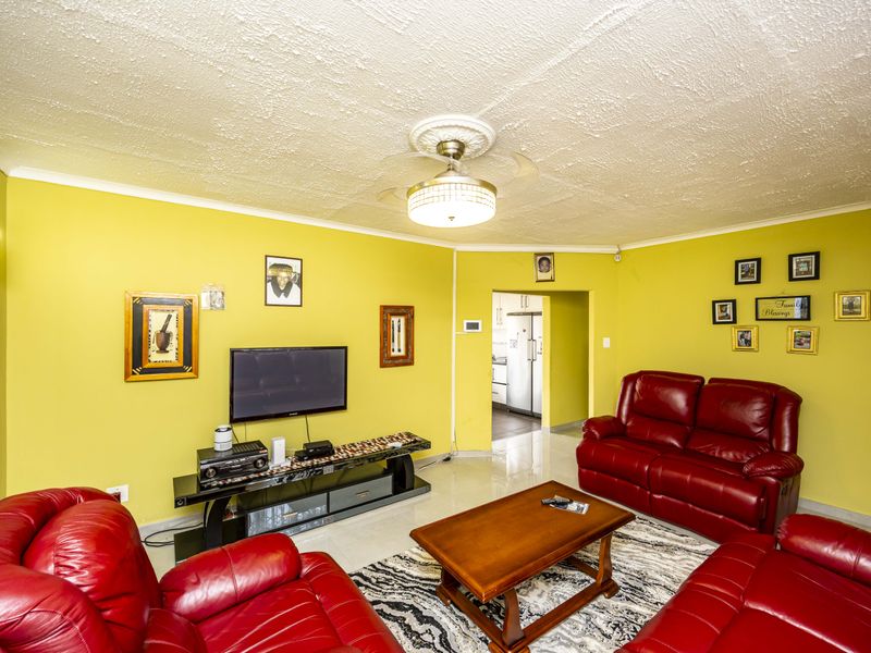 A living room featuring tiled flooring, a ceiling fan with a decorative rose, and wall sconce lighting, with a view into the adjacent kitchen area.