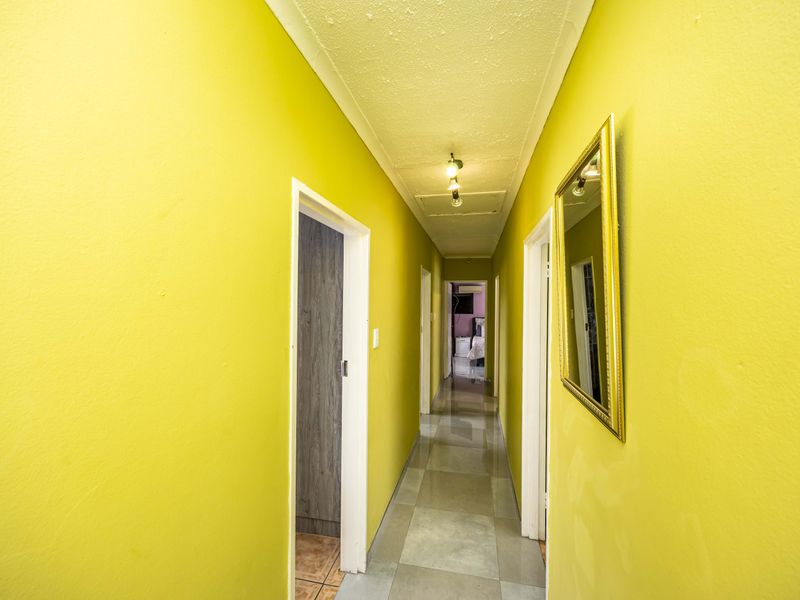 A long hallway featuring bright yellow walls, tiled flooring, and a ceiling access hatch, providing access to multiple rooms within the home.