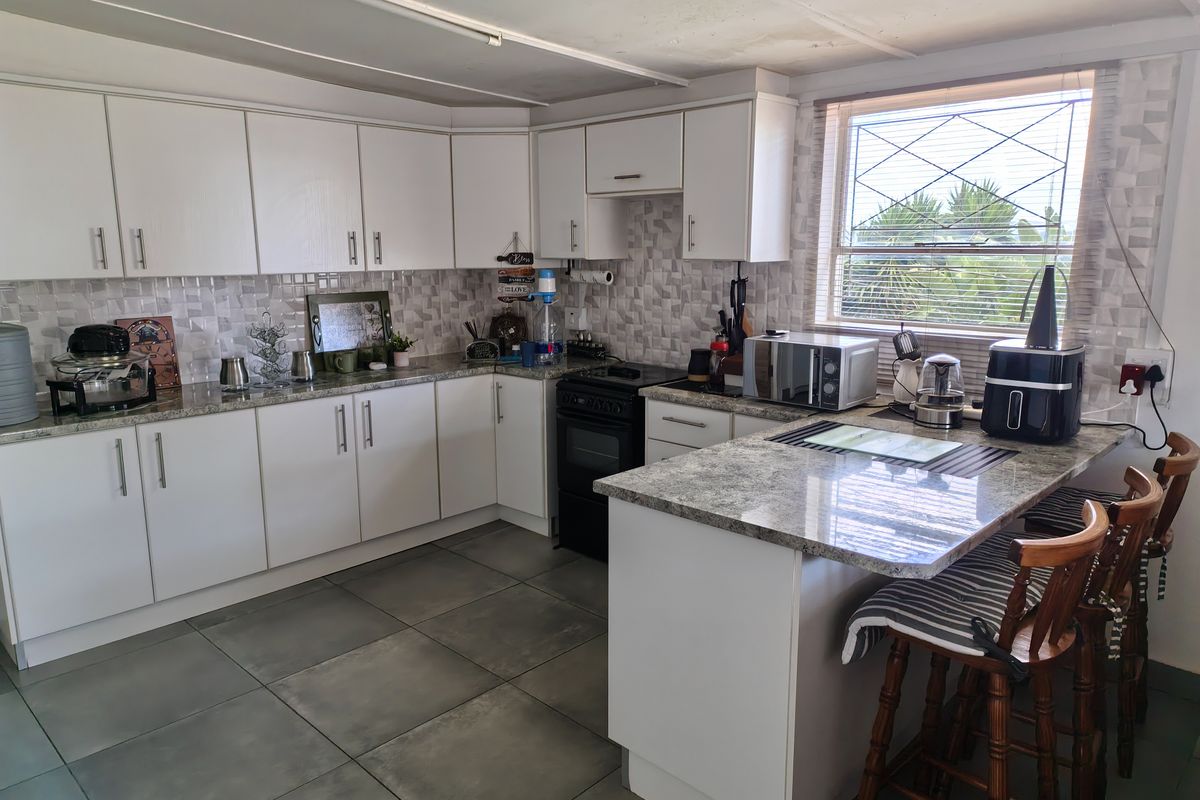 A functional kitchen featuring white cabinetry, granite countertops, a tiled backsplash, and a breakfast nook area with tiled flooring.