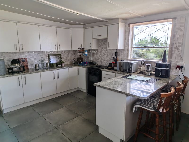 A functional kitchen featuring white cabinetry, granite countertops, a tiled backsplash, and a breakfast nook area with tiled flooring.