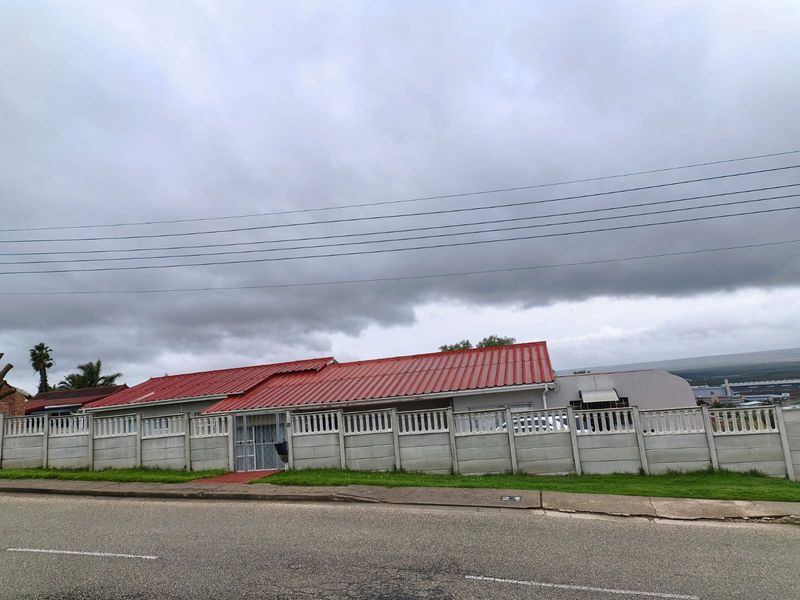 Front exterior view of a single-story house featuring a red corrugated metal roof and a secure precast concrete boundary wall.