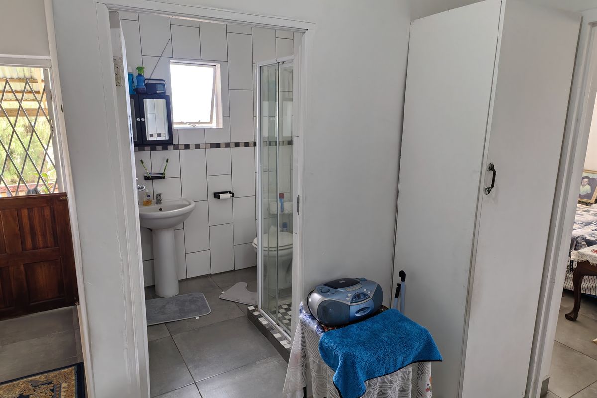 A functional bathroom featuring a pedestal basin, shower enclosure, and toilet, with neutral wall and floor tiling.