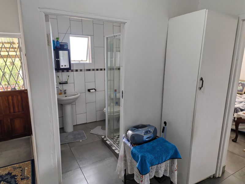 A functional bathroom featuring a pedestal basin, shower enclosure, and toilet, with neutral wall and floor tiling.