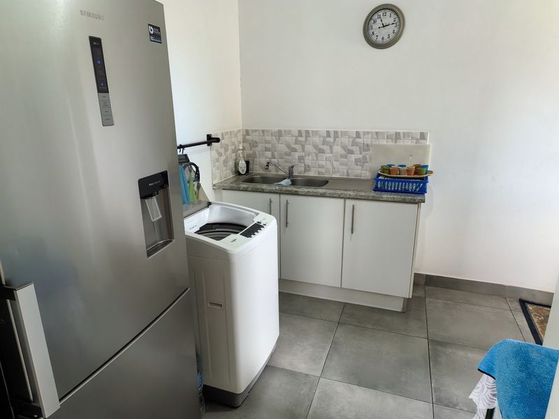 A functional laundry area featuring built-in cabinetry, a stainless steel sink, tiled backsplash, and durable floor tiles.