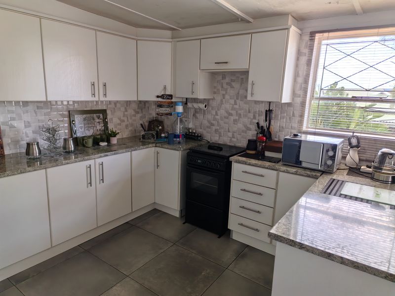 A functional kitchen featuring white cabinetry, granite-look laminate countertops, tiled backsplash, and a freestanding stove with tiled flooring.
