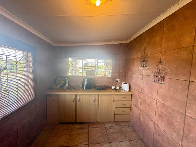 A functional kitchen area featuring built-in cabinetry, tiled walls, and tiled flooring, with security bars on the windows for added safety.