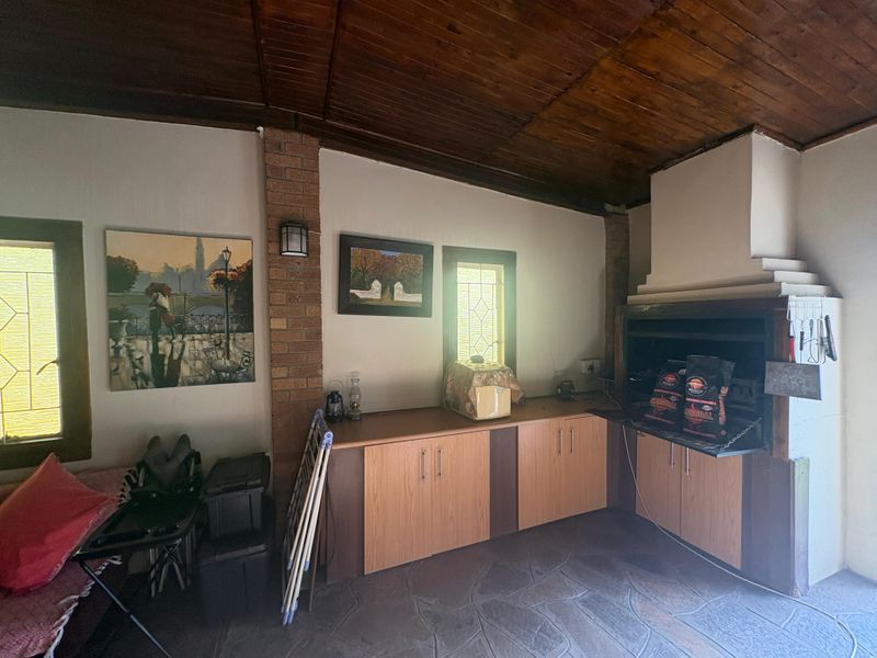Covered patio area featuring a built-in braai, timber ceiling, stone flooring, and integrated cabinetry, providing a functional space for outdoor entertaining.