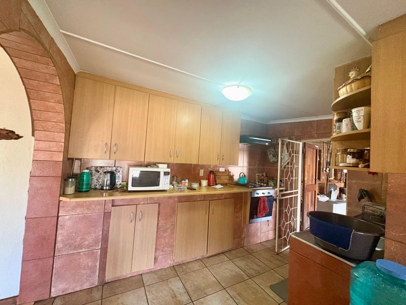 A dated kitchen featuring wood-look cabinetry, tiled splashbacks, and tiled flooring, with an integrated oven and extractor fan.