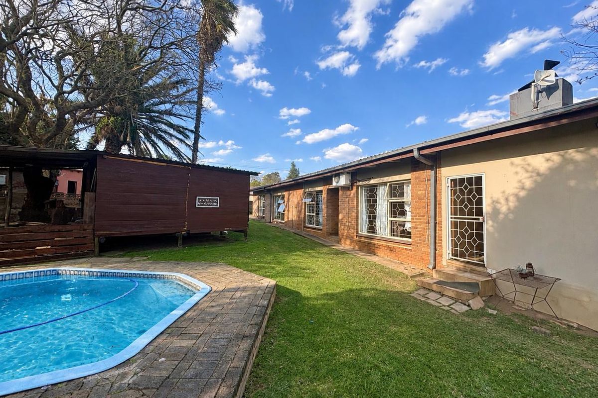 Rear exterior view featuring a swimming pool, paved surround, lawn area, and brick building facade with security gate and air conditioning unit.