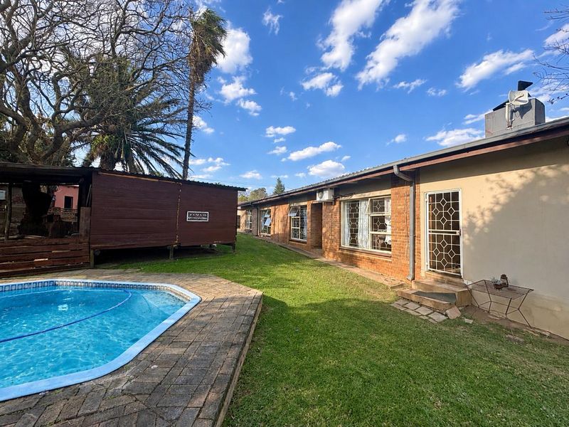 Rear exterior view featuring a swimming pool, paved surround, lawn area, and brick building facade with security gate and air conditioning unit.