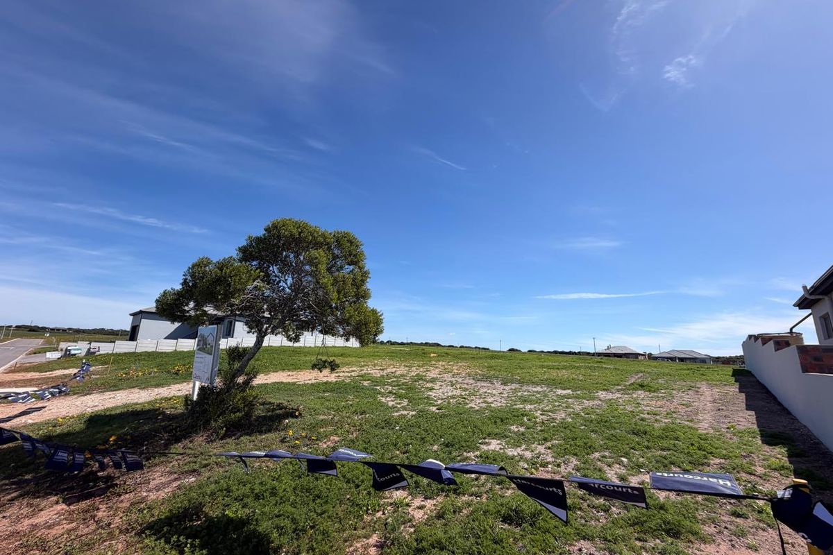 A wide-angle view of a vacant residential plot featuring natural grass coverage and a boundary wall, ready for development.