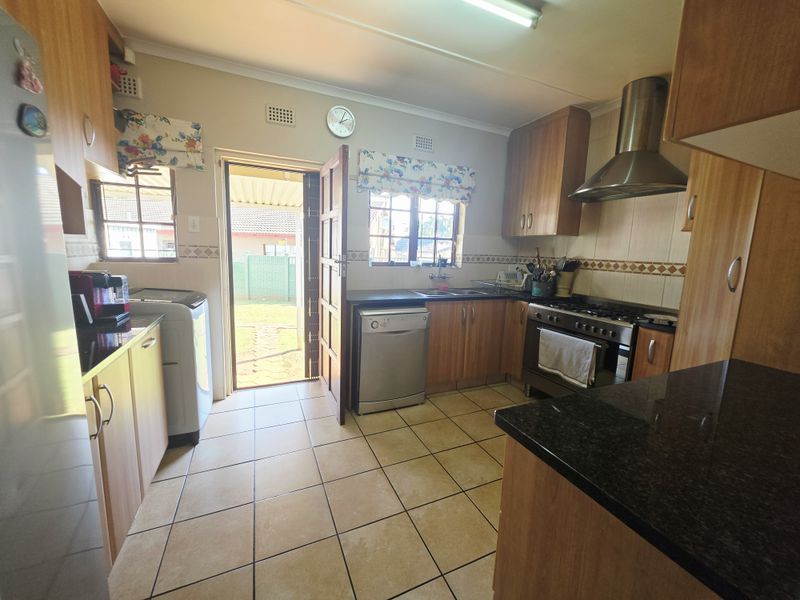 Functional kitchen featuring laminate cabinetry, granite countertops, a stainless steel extractor fan, gas stove, and direct access to the rear garden.
