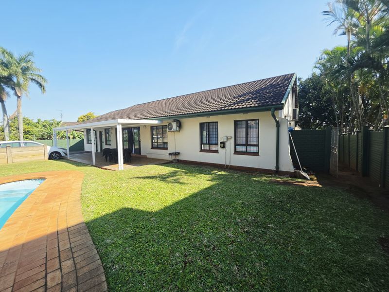 Rear view of the house featuring a covered patio, a swimming pool, and a well-maintained lawn area with boundary walling.