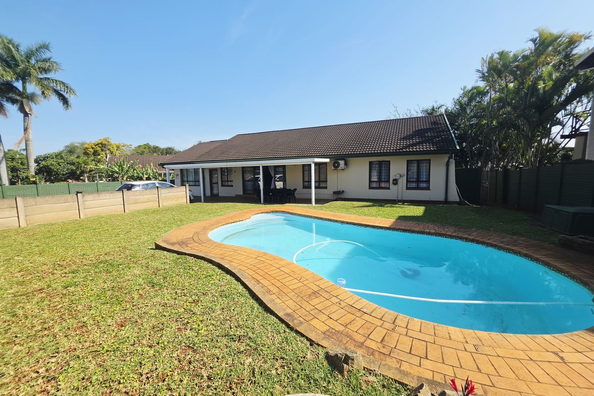 Rear view of the property featuring a swimming pool with brick coping, a covered patio area, and a well-maintained garden with boundary walling.