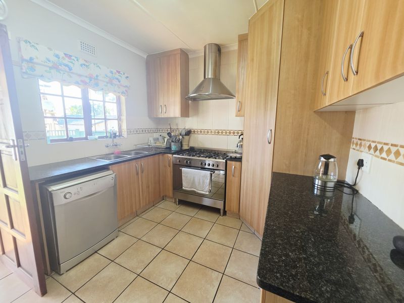 A functional kitchen featuring laminate cabinetry, granite countertops, a stainless steel gas stove with extractor fan, and tiled flooring.
