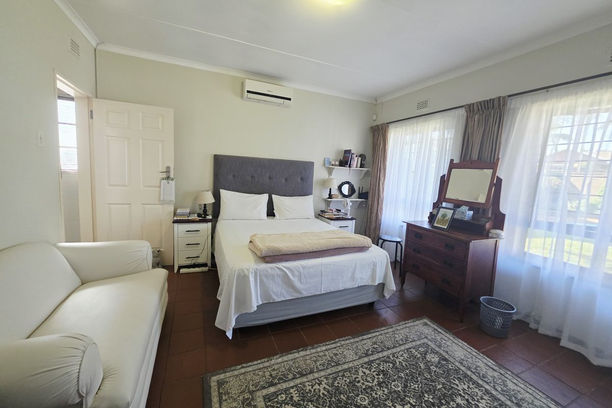 A well-lit bedroom featuring tiled flooring, an integrated air conditioning unit, and large windows with curtain rails, offering a comfortable and functional living space.