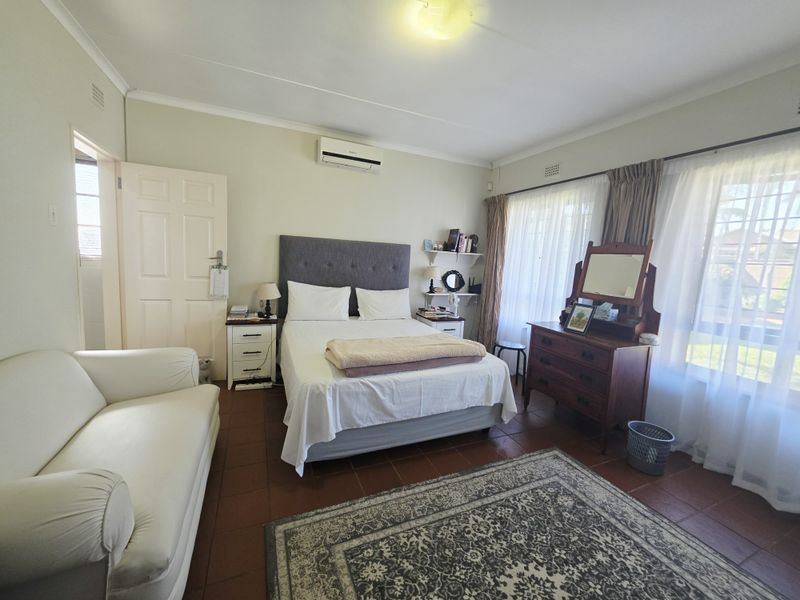 A well-lit bedroom featuring tiled flooring, an integrated air conditioning unit, and large windows with curtain rails, offering a comfortable and functional living space.
